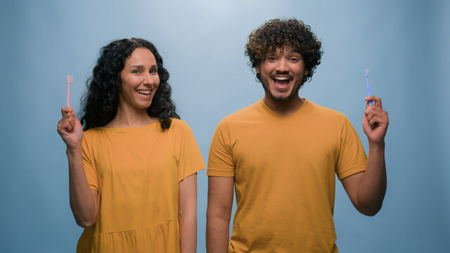Multiracial couple Hispanic woman girl and Indian man Arabian guy holding tooth brush pretend brushing teeth dental care using toothbrushes oral hygiene healthcare whitening at blue studio background