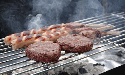 Smoke rising from burgers, sausages and lamb chops cooking on a barbeque grill. 