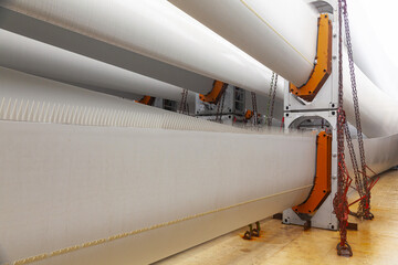 Blades from wind turbines laid in special fasteners and chained on the deck of the ship for their transportation by sea on a ship.