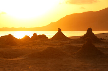 Orange dawn on the ocean shore on a wild beach. Sand pyramids made by crabs on the shore. Calm sea and rocky mountains.
