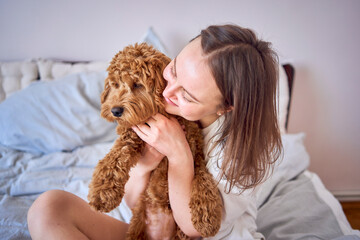 young woman playing and kissing cockapoo girl on bed, minimalism