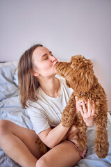 young woman playing and kissing cockapoo girl on bed, minimalism