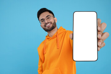 Happy man holding smartphone with empty screen on light blue background, space for text