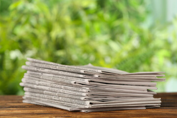 Stack of newspapers on wooden table against blurred green background. Journalist's work