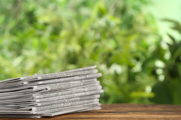 Stack of newspapers on wooden table against blurred green background, space for text. Journalist's...