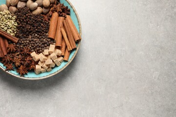 Different spices and nuts in bowl on light gray textured table, top view. Space for text