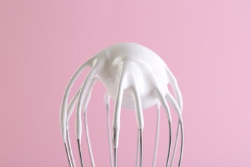 Whisk with whipped cream on pink background, closeup