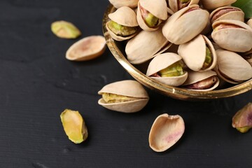 Tasty pistachios in bowl on black table, closeup. Space for text
