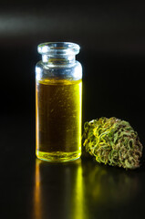 still life of dried marijuana buds and small glass transparent bottle filled with cannabis infused olive oil on black background