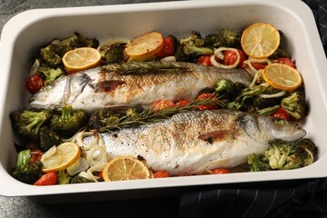 Delicious fish with vegetables and lemon in baking dish on table