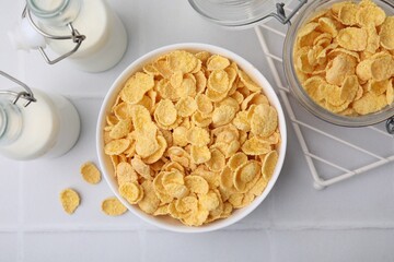 Tasty crispy corn flakes and milk on white tiled table, flat lay. Breakfast cereal