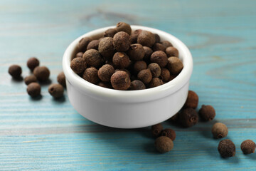 Aromatic allspice pepper grains in bowl on light blue wooden table, closeup