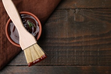 Marinade in bowl and basting brush on wooden table, top view. Space for text