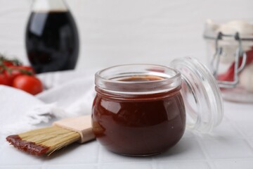 Marinade in jar and basting brush on white tiled table, closeup