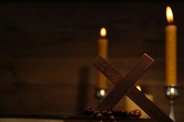 Wooden cross, rosary beads and church candles against blurred background, space for text