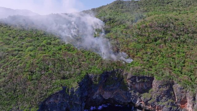 Fire smoke in forest of Cabo Cabron National Park along high cliffs, Samana in Dominican Republic. Aerial drone view