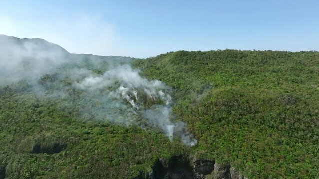 Fire smoke in lush forest along cliffs of Cabo Cabron National Park, Samana in Dominican Republic. Aerial birdseye