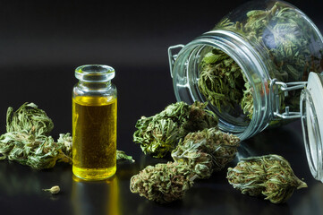 noir still life of hemp products consist of dry flowers of medical marijuana, glass jar with buds, cannabis seeds and small bottle with CBD infused oil close up on black background