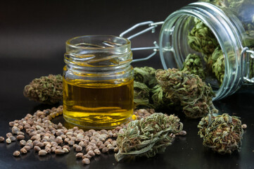 noir still life of hemp products consist of dry flowers of medical marijuana, glass jar with buds, cannabis seeds and small bottle with CBD infused oil close up on black background