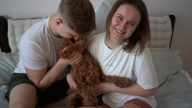 young couple gently playing with cockapoo on bed in bedroom, minimalism