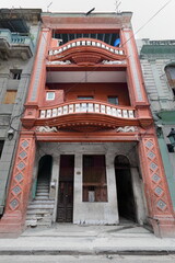 Fototapeta na wymiar Dilapidated Centro Havana tenement house in Eclectic style painted reddish-orange from the early 1900s with undulating balconies. La Habana-Cuba-075