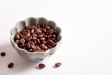Coffee beans into bowl on white table. Top view. Soft focus
