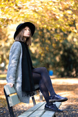 Young girl in a hat sitting on a bench in the autumn park
