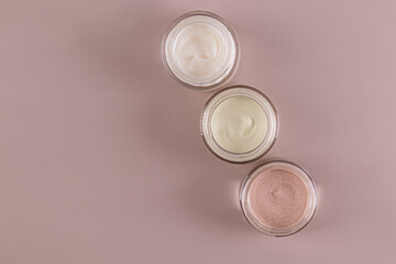 A jars with cosmetic cream of different textures and colors for face and body skin care. Beige background. space for text. Top view.