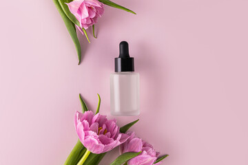 Obraz na płótnie Canvas Cosmetic product, oil, serum for face or body skin care in a matte cosmetic bottle on a purple background with delicate spring flowers.