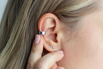 Cuff earring. Cropped shot of a young blonde woman showing silver earring with finger. Jewelry, accessories - obrazy, fototapety, plakaty