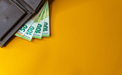 Top view of New brown genuine leather wallet with banknotes and credit card inside isolated on orange background