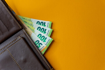 Top view of New brown genuine leather wallet with banknotes and credit card inside isolated on orange background