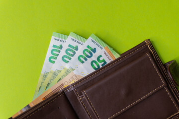 Top view of New brown genuine leather wallet with banknotes and credit card inside isolated on orange background