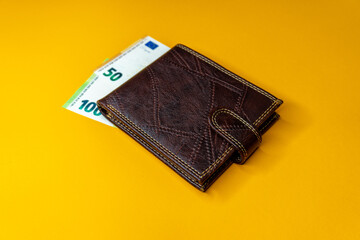 Top view of New brown genuine leather wallet with banknotes and credit card inside isolated on orange background