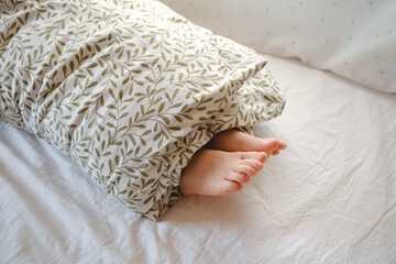 Rolled person. A child wrapped in a blanket with sticking out feet lies on the bed in the bedroom. Sunny morning dream. Psychology comfort. Toes up. High quality - obrazy, fototapety, plakaty