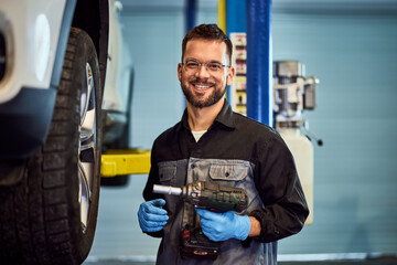 Portrait of a smiling mechanic working at his garage, holding a drill. - 756408402