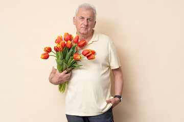 Handsome senior man with a bouquet of tulips on a cream background in the studio.