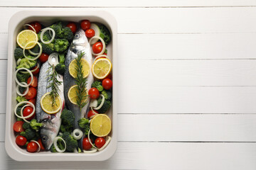 Raw fish with vegetables and lemon in baking dish on white wooden table, top view. Space for text