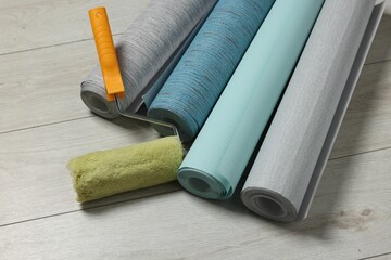 Different wallpaper rolls and roller on floor