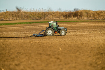 Obraz premium Tractor with a plow attachment works the soil in agricultural farmland during golden hour