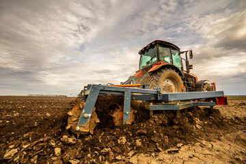 Agricultural scene of a tractor plowing dry soil, kicking up dust with a dramatic sky overhead - obrazy, fototapety, plakaty