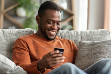A smiling African American man is at home, sitting on the sofa, holding a credit card and using a mobile phone. Close-up photo, Generative AI