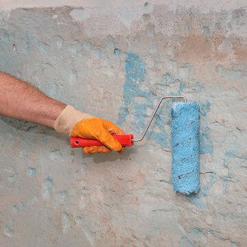 Hand of worker using paint roller to apply adhesive primer fluid for gluing tiles