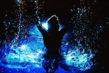 Woman in swimming pool splashing water all around. Nightlife party background. Artistic contrast photograph. Bluecolor pool. Swimming in water.