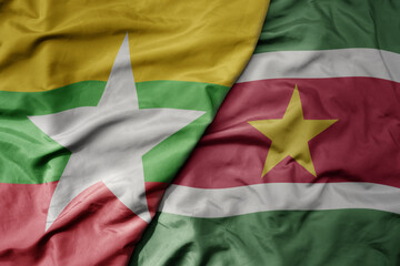 big waving national colorful flag of suriname and national flag of myanmar .