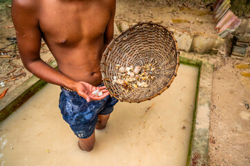 Boy in muddy water hold washed mined gemstone and rattan pan. - 756431618