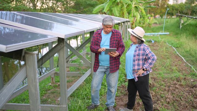 Old Asian couple farmers use tablets to adjust solar cells degree and check solar cell performance after rain and Dust and dirt stains on the solar cell. Concept of farming technology.