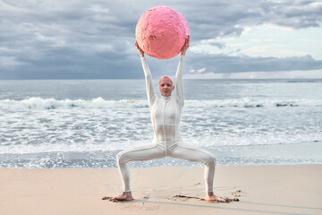 Hairless performer girl with alopecia in white futuristic suit dancing with pink sphere at sea, metaphoric surreal scene exudes confidence, unique beauty and hope resilience against life challenges