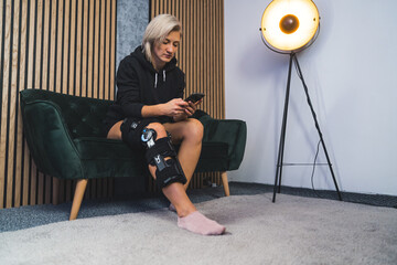 woman treating herself at home, wearing a knee brace and scrolling the phone. High quality photo