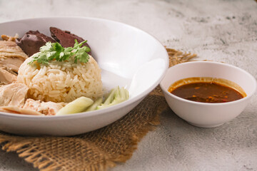 Hainanese chicken rice with coriander, cucumber and chicken soup on black background. Local food in East and Southeast Asia